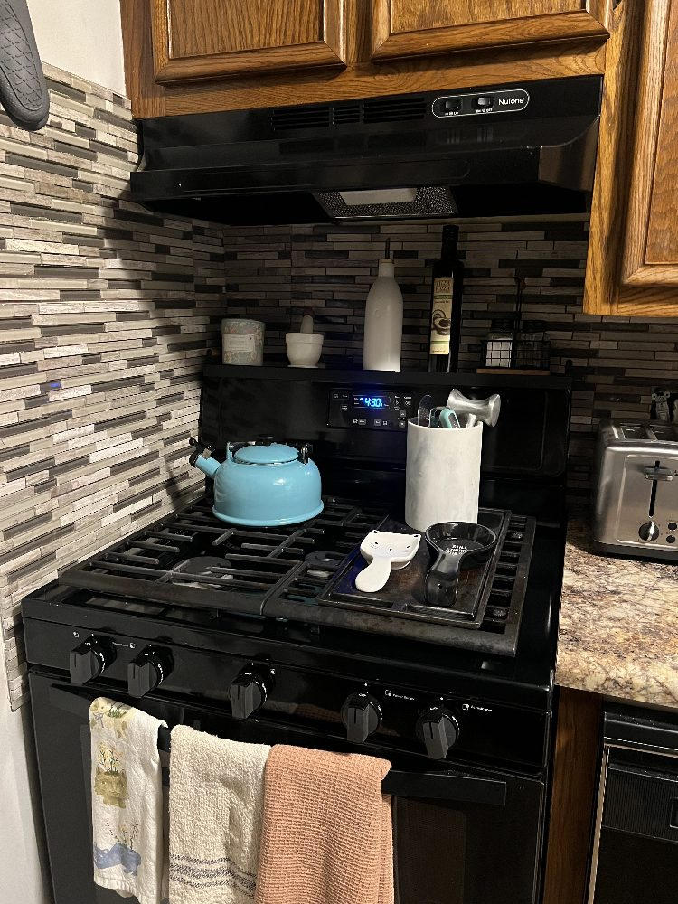 Black gas stove with a blue kettle and various utensils on the counter
